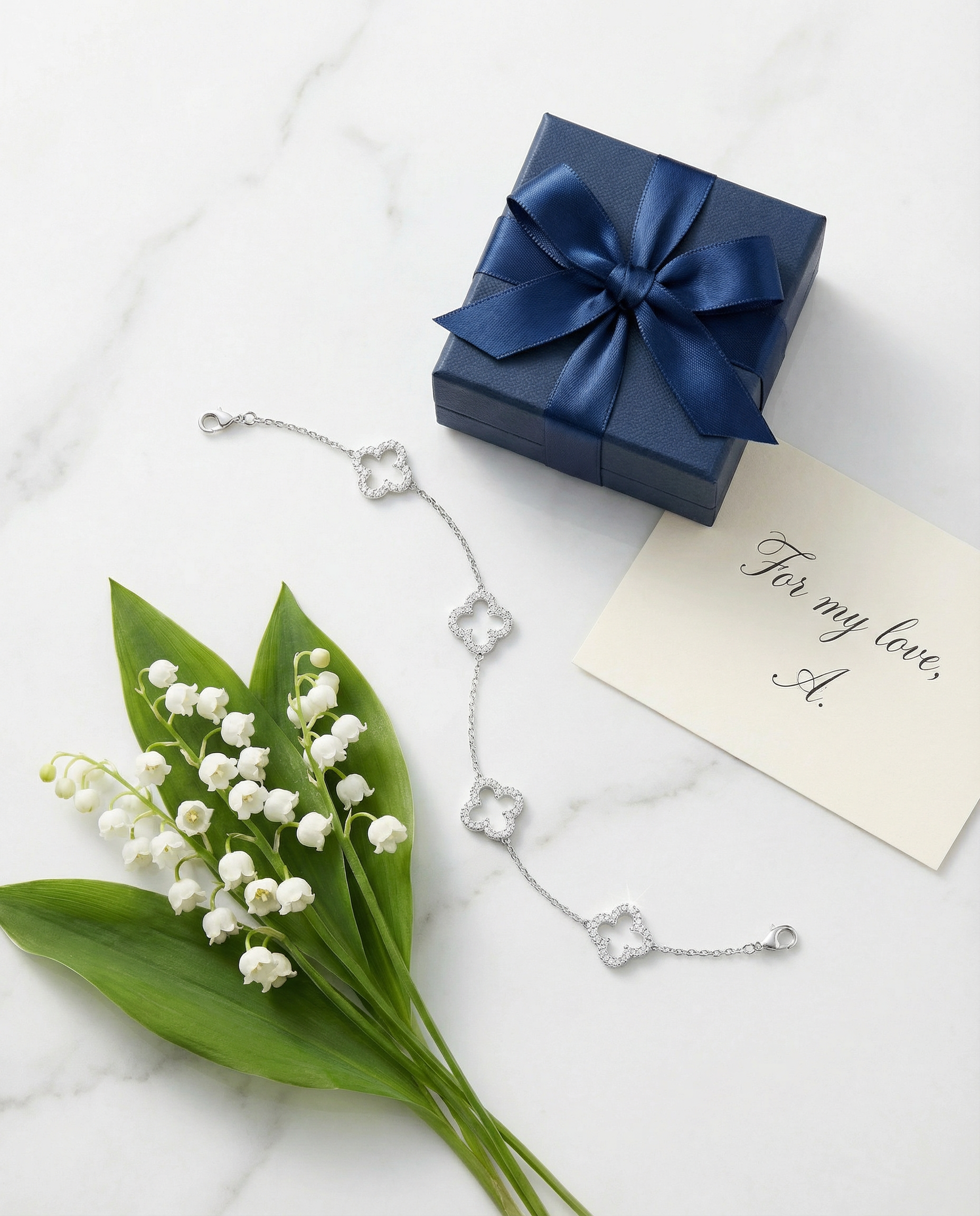 Bracelet Trèfle — Flat lay marbre blanc avec boîte cadeau navy et muguet